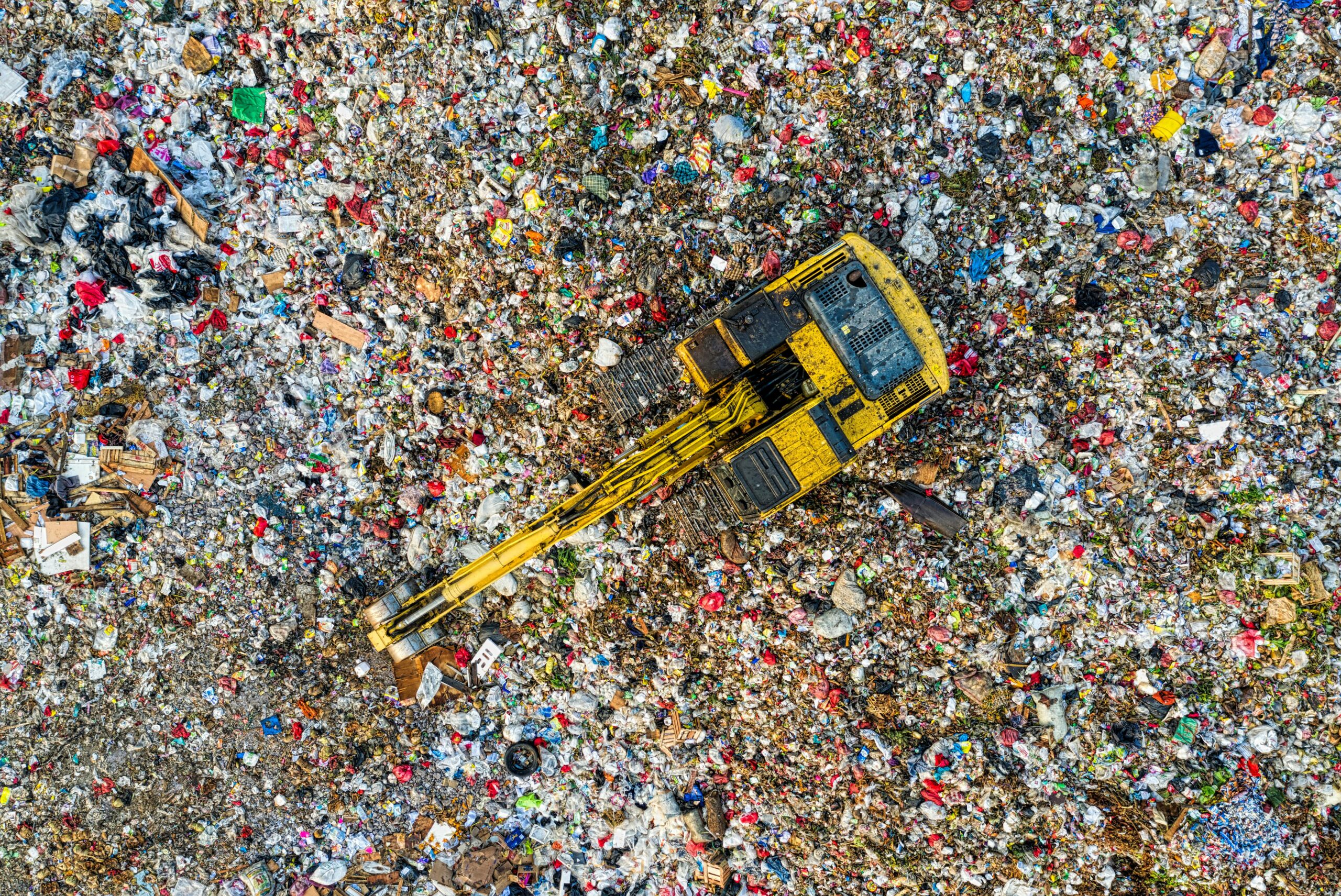 A birds eye view of a landfill with a backhoe moving the garbage